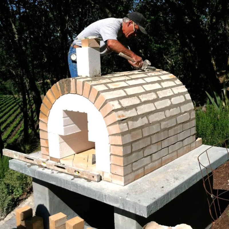 A builder laying full-size fire brick to form the arch of a backyard brick pizza oven