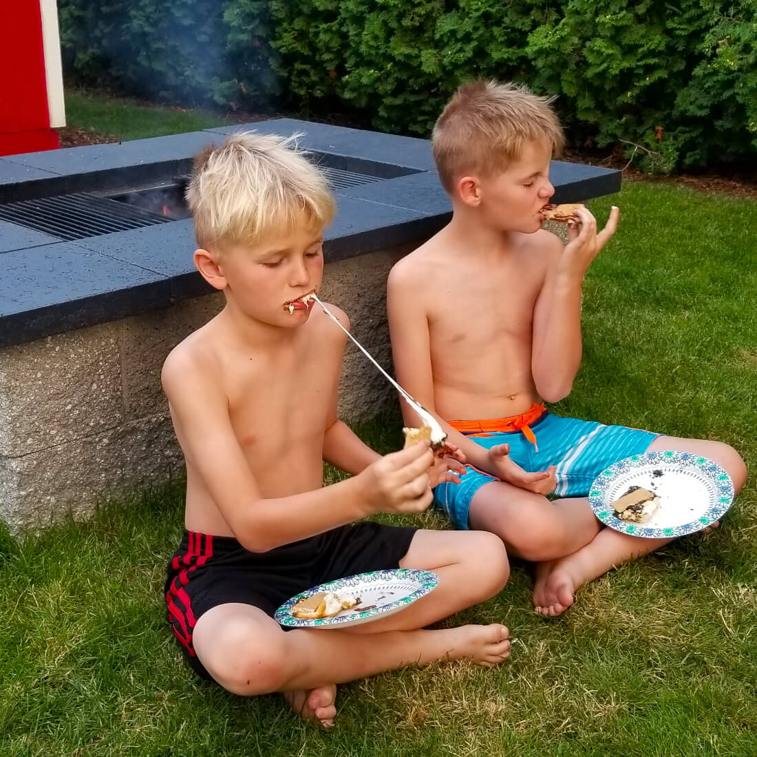 Kids eating s'mores beside a backyard fire pit grill