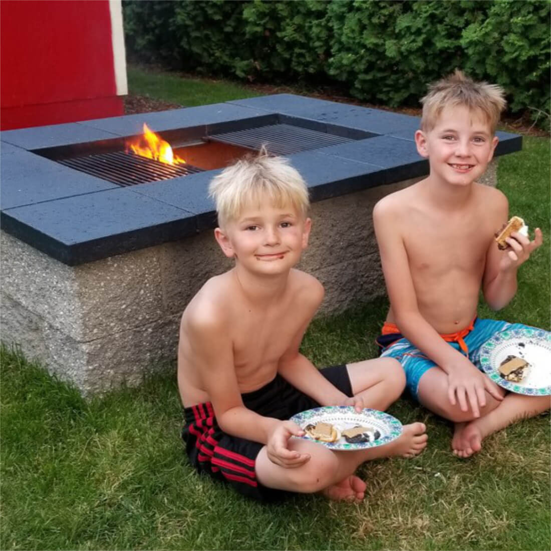 Kids eating dinner by a cinder block fire pit grill with an open wood fire