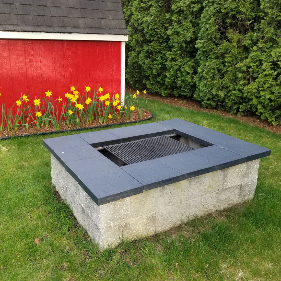 Finished rectangular fire pit with grill built from cinder blocks and concrete pavers