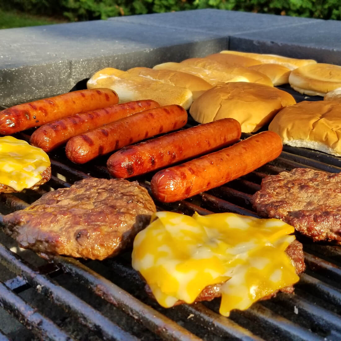 Hot dogs and cheeseburgers grilling on a wood-fired fire pit grill